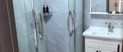 Un baño moderno con ducha envuelta en vidrio, un lavabo blanco y un espejo sobre él.