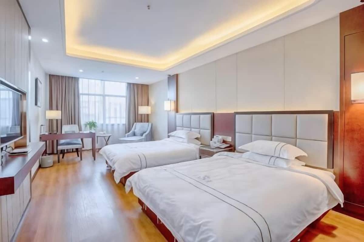 A hotel room with two beds, a desk, a chair, and a TV.