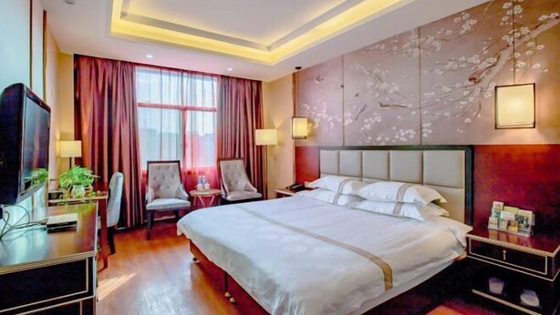 Quarto de hotel com uma cama grande, uma mesa com computador, uma cadeira, uma TV e um mural floral na parede.