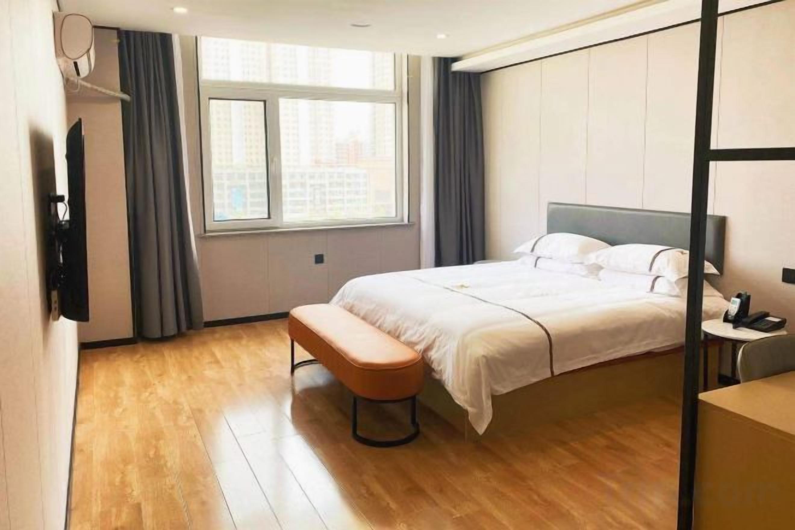 A hotel room with a bed, a bench, a desk, and a window.