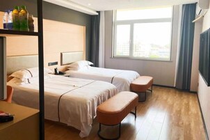 Quarto de hotel com duas camas, um banco, uma escrivaninha e uma janela com vista.