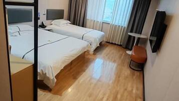 A hotel room with two beds, a bedside table, a chair, a small table, and a window with curtains.