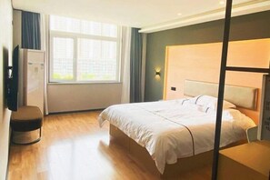 A hotel room with a bed, a desk, a chair, a window, and a wall-mounted TV.