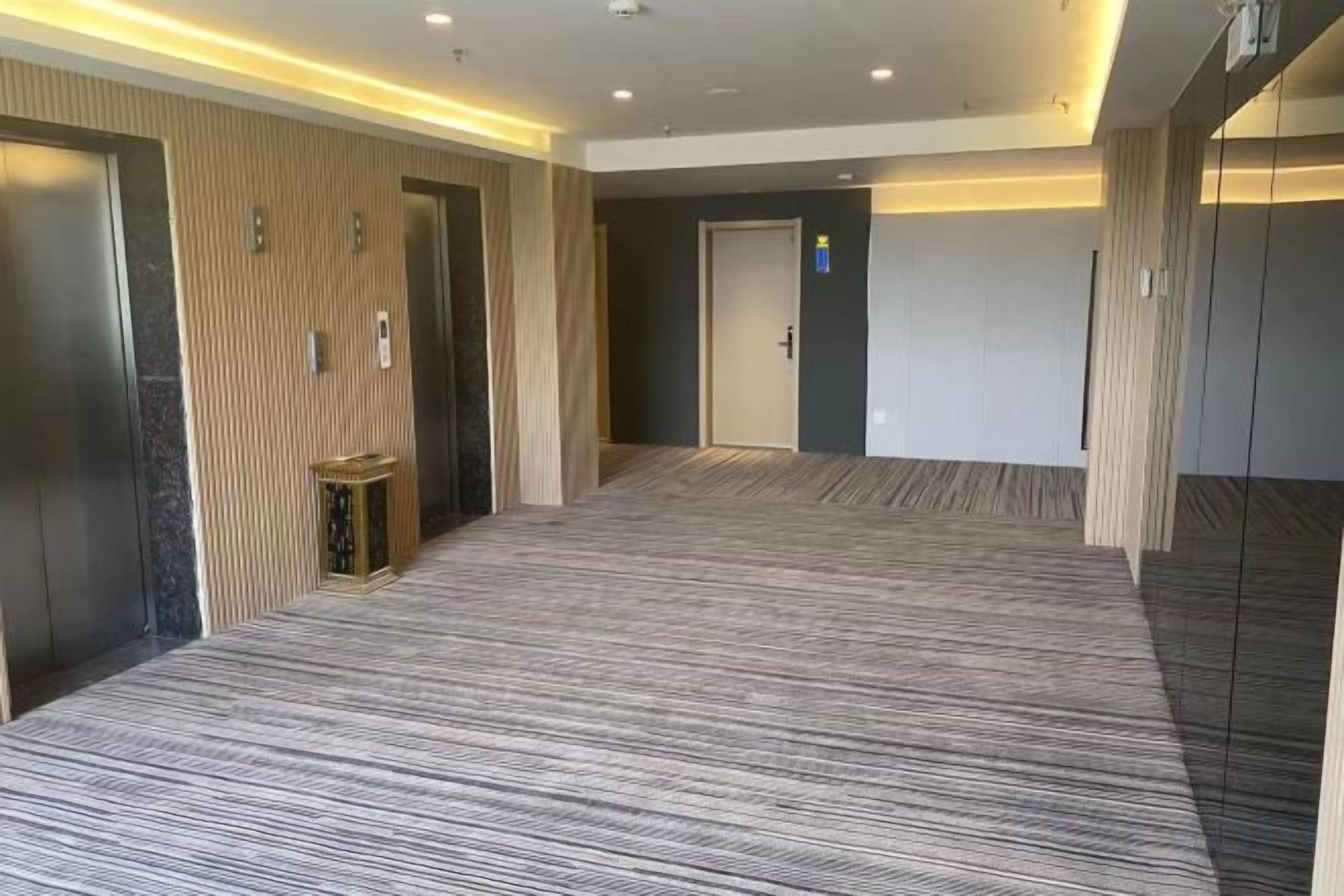 A hotel corridor with carpeted flooring, wooden paneling, and a door at the end.