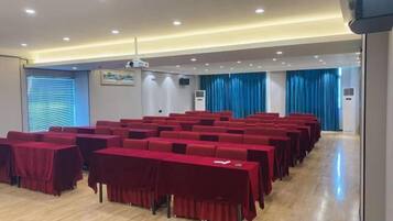 A conference room with rows of tables and chairs, a projector, and a blue curtain backdrop.