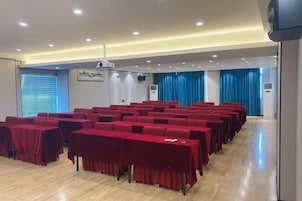 A conference room with rows of tables and chairs, a projector, and a blue curtain backdrop.