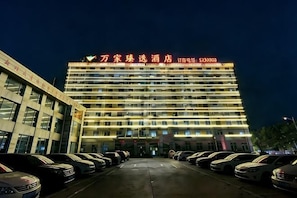 A multi-story hotel with a row of parked cars in front. - Wanjia Zhenxuan Hotel (long distance bus station) (Tengzhou)