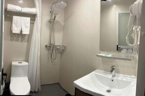 A bathroom with a toilet, shower, sink, and a hairdryer mounted on the wall.