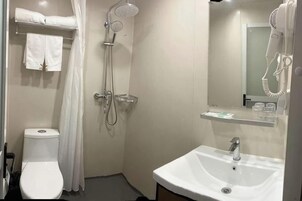 A bathroom with a toilet, shower, sink, and a hairdryer mounted on the wall.