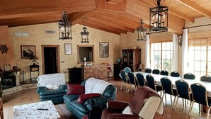 Ein geräumiges Zimmer mit Kamin, einem Essbereich mit langem Tisch und Stühlen sowie einer gemütlichen Sitzecke mit Sofas und einem gemusterten Tischläufer.