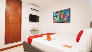 Una habitación de hotel con cama, televisión, aire acondicionado, un cuadro y una puerta.