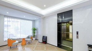A modern lobby with a tiled floor, two orange and grey chairs, a potted plant, and an elevator. - Jiada Hotel (Zhuhai Lovers Road Seaside Swimming Pool) (Zhuhai)