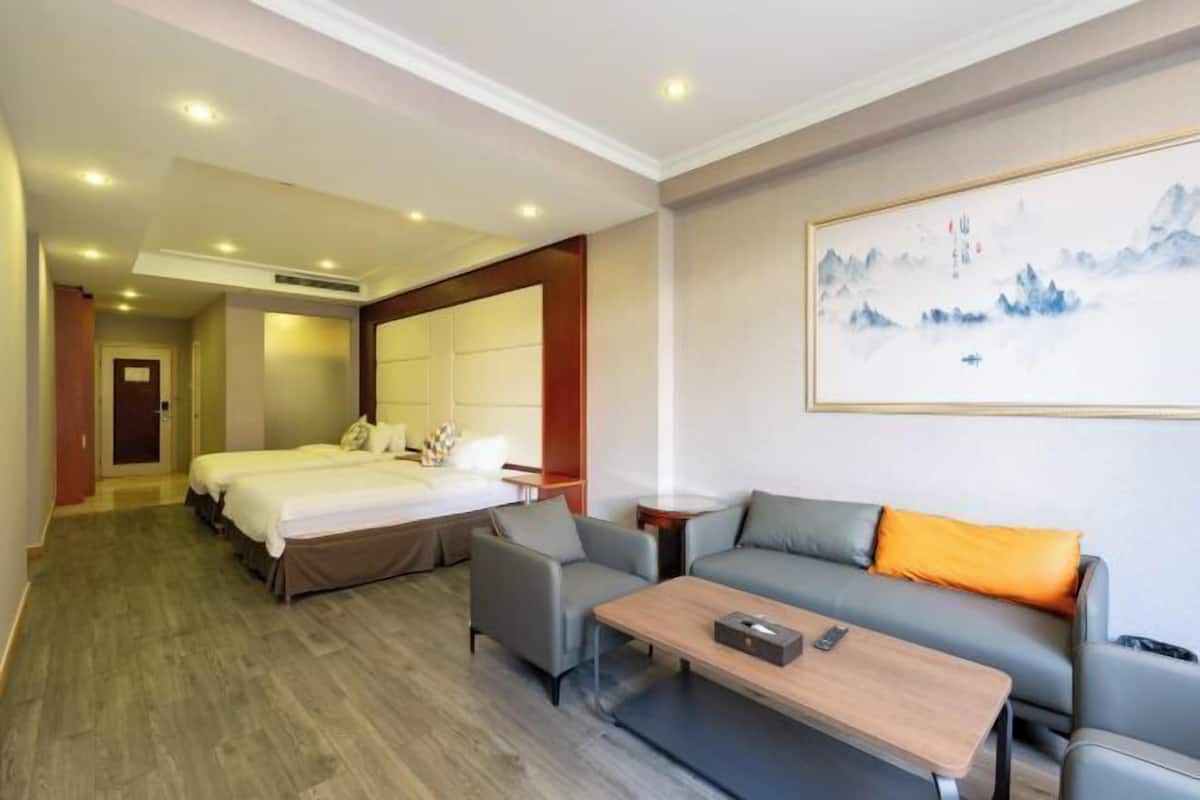 A hotel room with a bed, a sofa, a coffee table, and a painting on the wall.