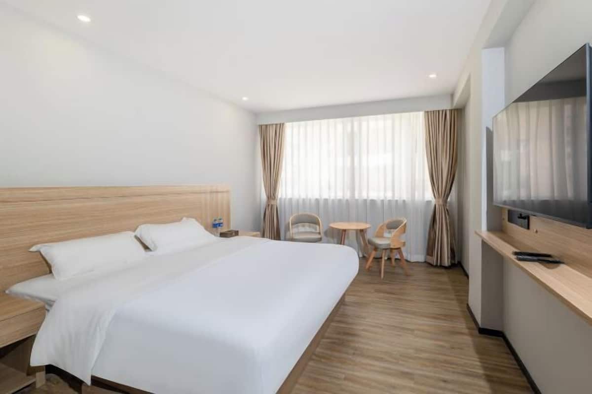 A hotel room with a large bed, a desk with a TV, a chair, and a small table.