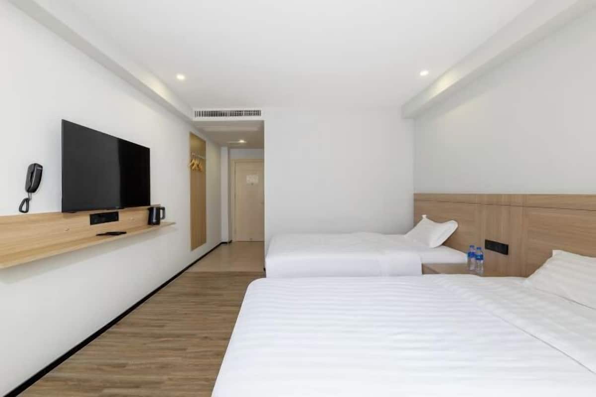 A hotel room with two beds, a TV on a wooden shelf, a phone, and a door leading to another room.