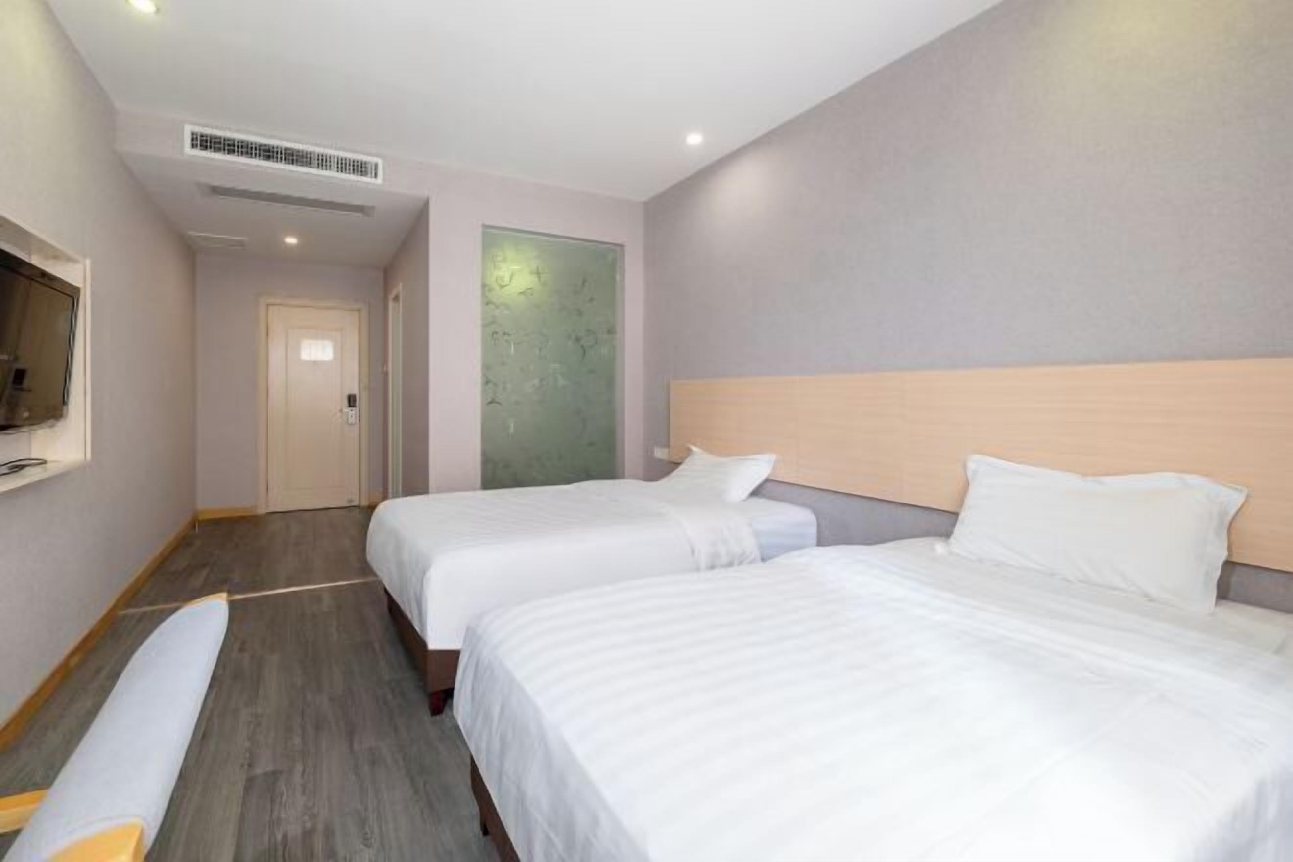 A hotel room with two beds, a television, a door, and a wall with a textured pattern.