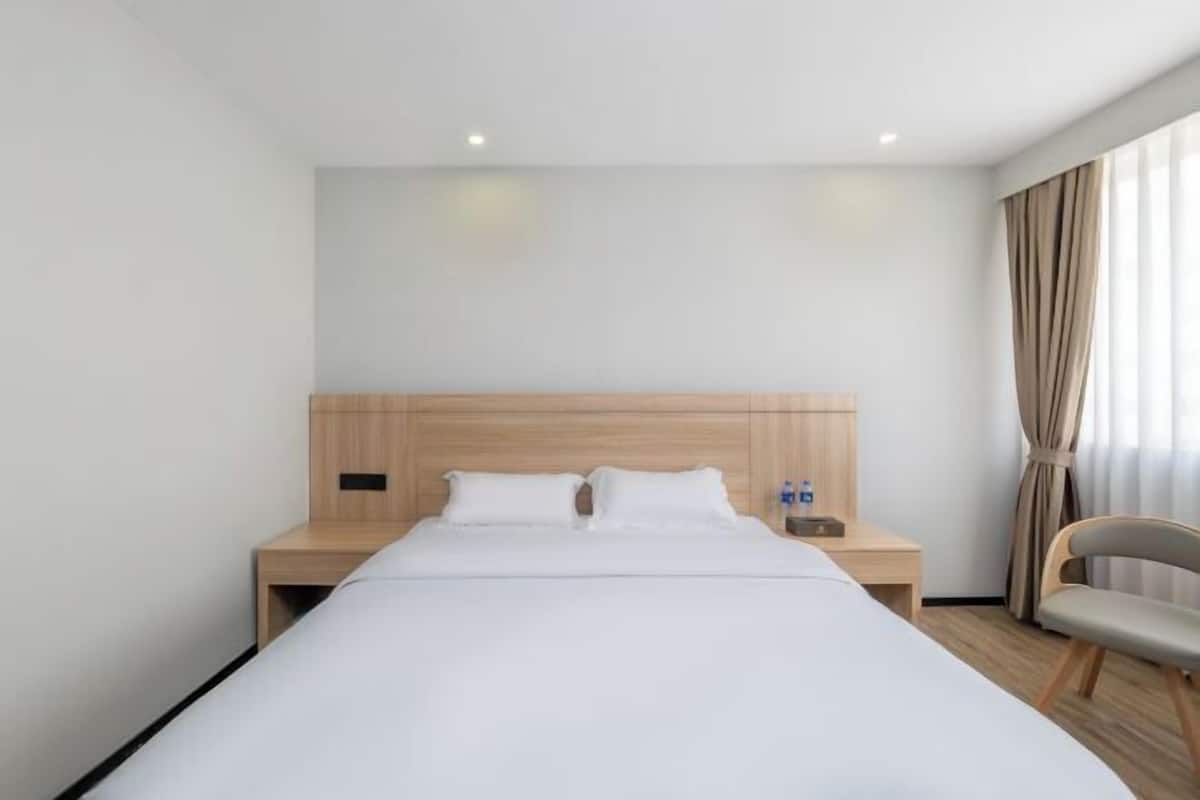 A hotel room with a large bed, wooden headboard, bedside tables, a chair, and a window with curtains.