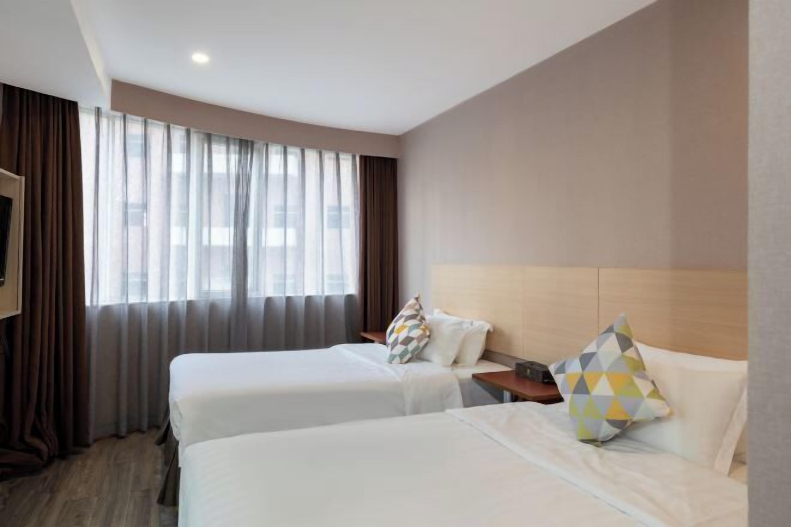 Une chambre d’hôtel avec deux lits, une télévision et une grande fenêtre avec des rideaux.