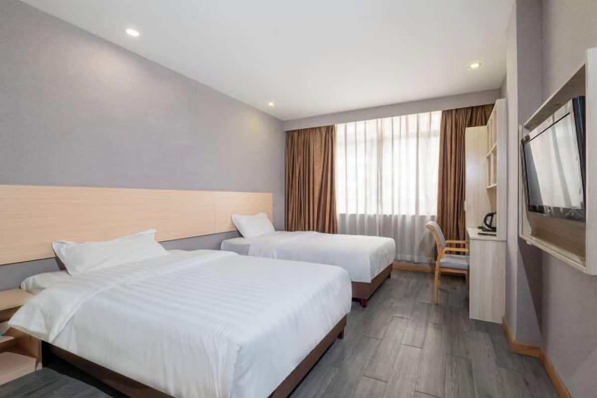 A hotel room with two beds, a desk, a chair, a TV, and a window with curtains.