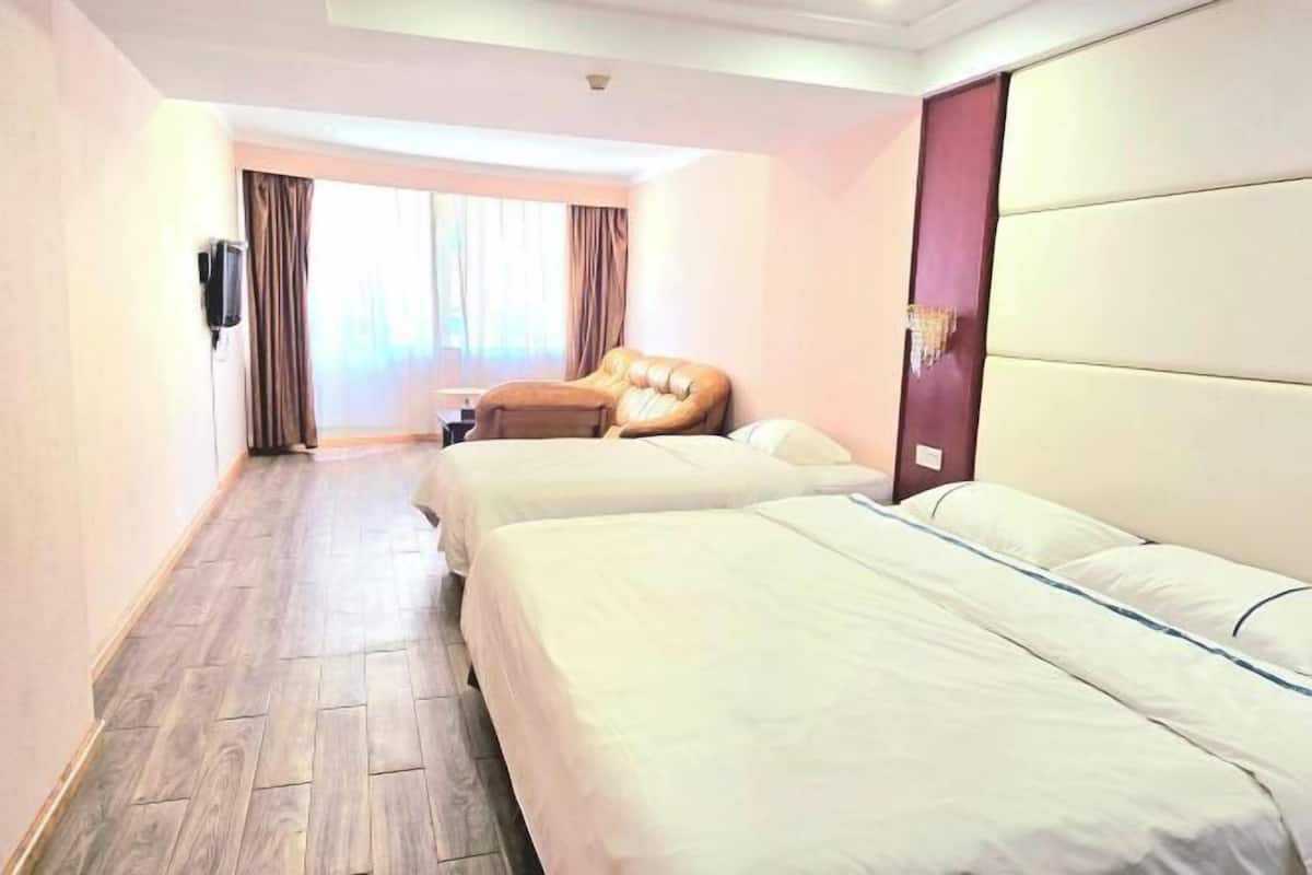 A hotel room with two beds, a sofa, a TV, and a window with curtains.