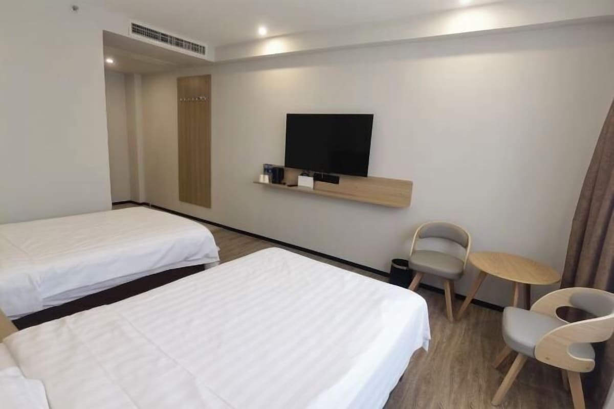 A hotel room with two beds, a TV mounted on the wall, a small table, and two chairs.