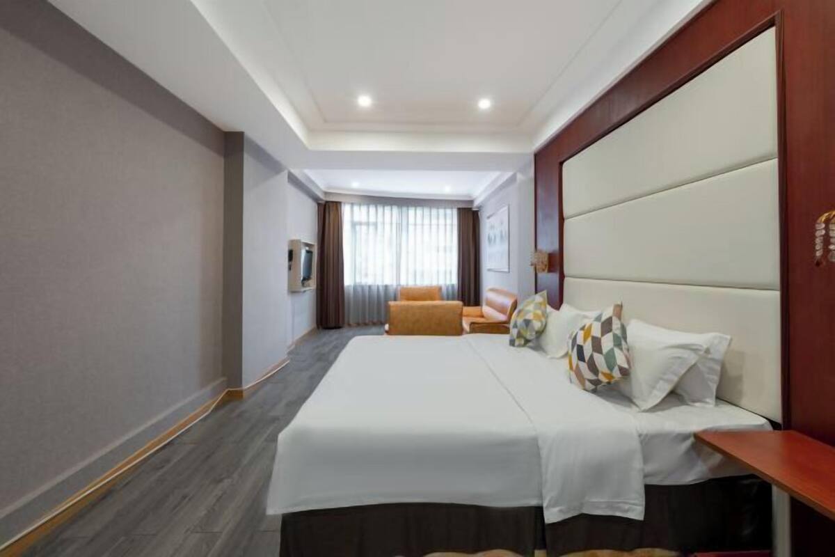 A hotel room with a large bed, a sofa, and a TV.