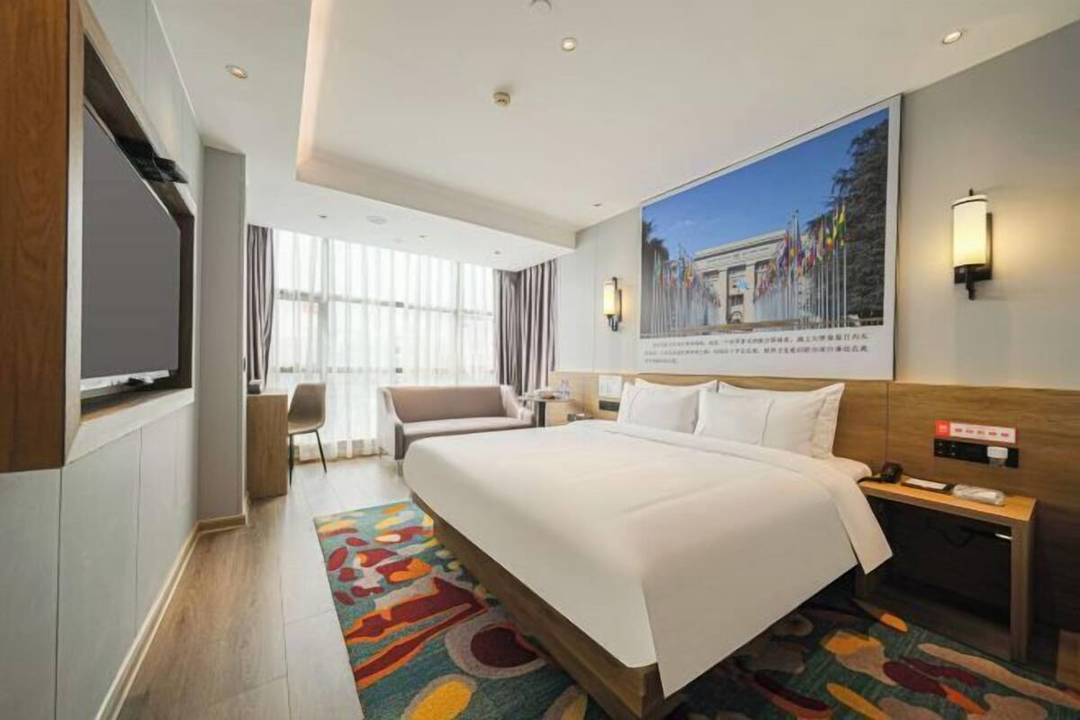 Une chambre d’hôtel avec un grand lit, un bureau, une chaise, une télévision et une grande fenêtre avec des rideaux.