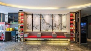 A modern reception area with a marble wall, red seating, and a desk with a computer. - The Sussie Hotel (Quanzhou Fengze Yunlu) (Quanzhou)