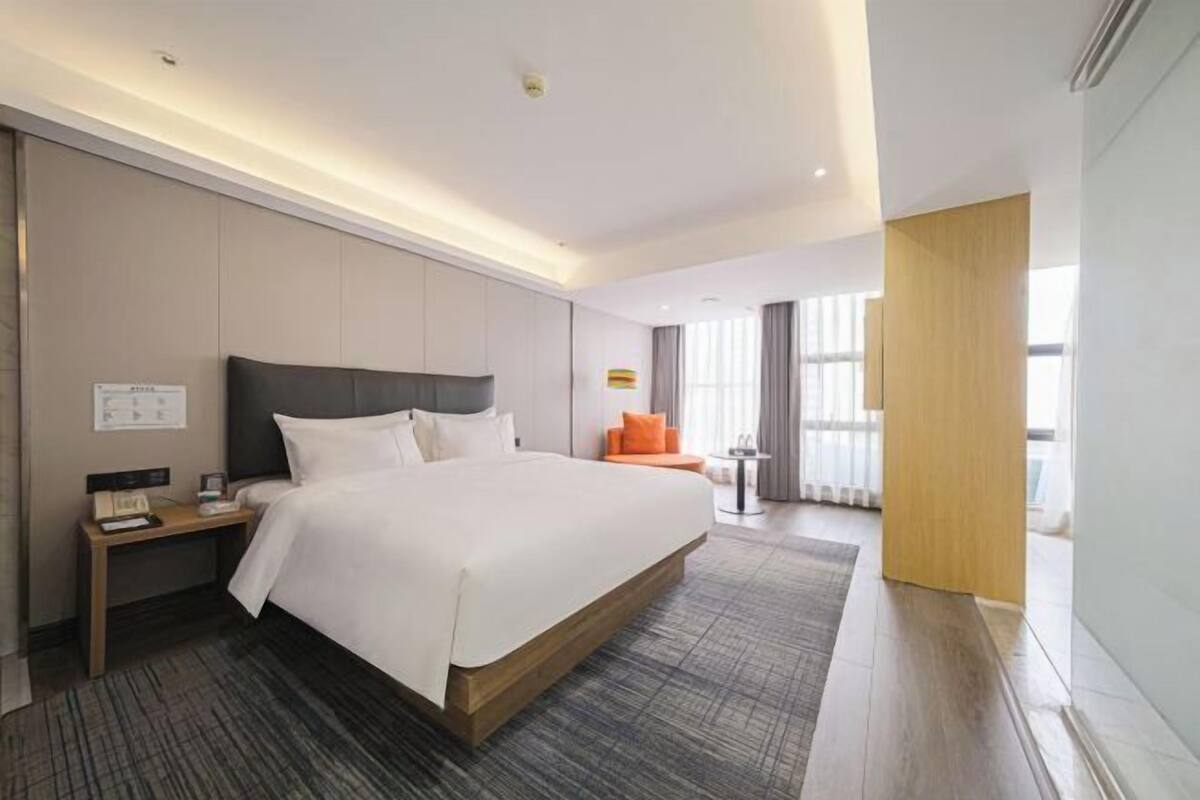Une chambre d’hôtel avec un grand lit, une table de chevet, un petit coin salon et une vue sur l’extérieur.