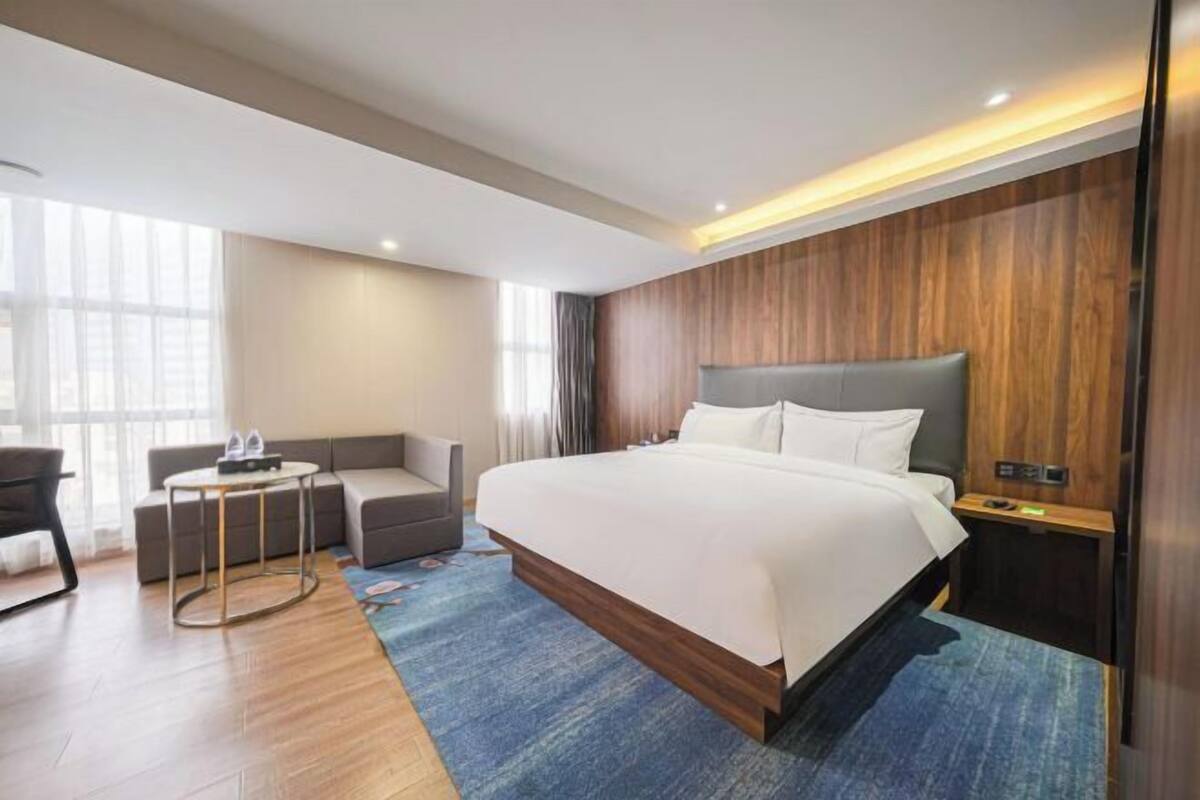 Une chambre d’hôtel moderne dotée d’un grand lit, d’un coin salon avec une table et offrant une vue sur la ville grâce à de grandes fenêtres.