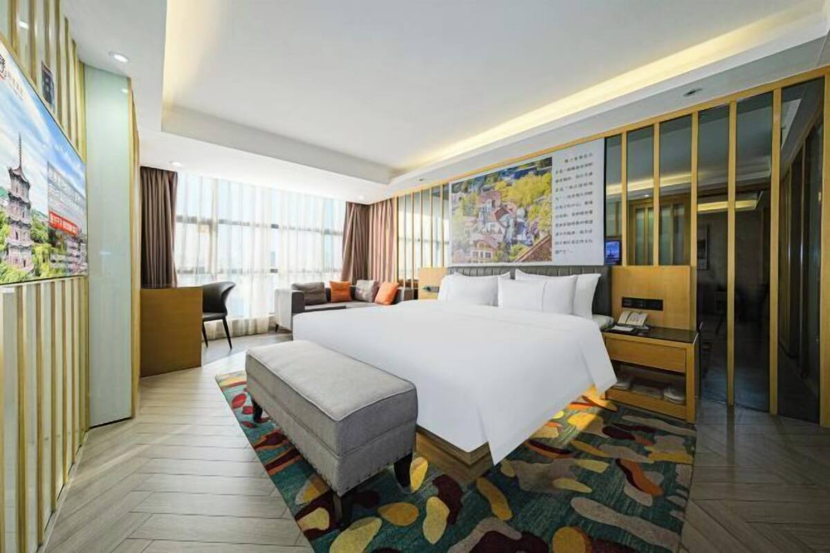 Une chambre d’hôtel avec un grand lit, un bureau, une chaise, une petite table et un tapis coloré.