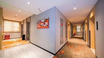 A hotel corridor with a patterned carpet, a framed poster on the wall, and a door with a sign.