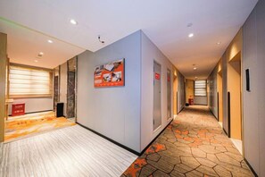 A hotel corridor with a patterned carpet, a framed poster on the wall, and a door with a sign. - The Sussie Hotel (Quanzhou Fengze Yunlu) (Quanzhou)