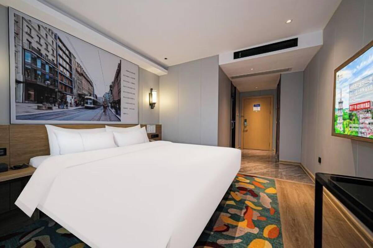 Une chambre d’hôtel avec un grand lit, une télévision, une œuvre d’art accrochée au mur et un sol recouvert de moquette.