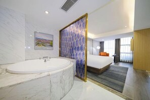 A modern hotel room with a marble bathtub, a large bed, and a view of the city.