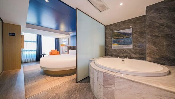 A modern hotel room with a large bed, a separate bathroom with a jacuzzi, and a view of the sea through a glass wall. - The Sussie Hotel (Quanzhou Fengze Yunlu) (Quanzhou)