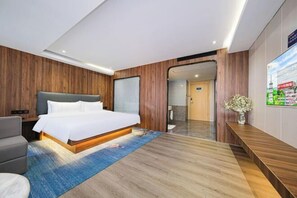 A modern hotel room with a large bed, a wooden accent wall, a flat-screen TV, and a wooden bench.