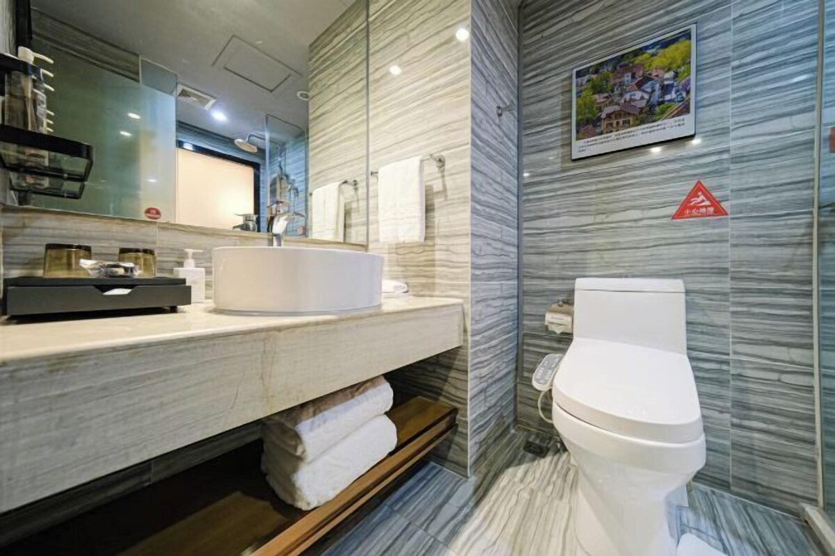 A modern bathroom with a marble backsplash, a round sink, a toilet, and a shower area.