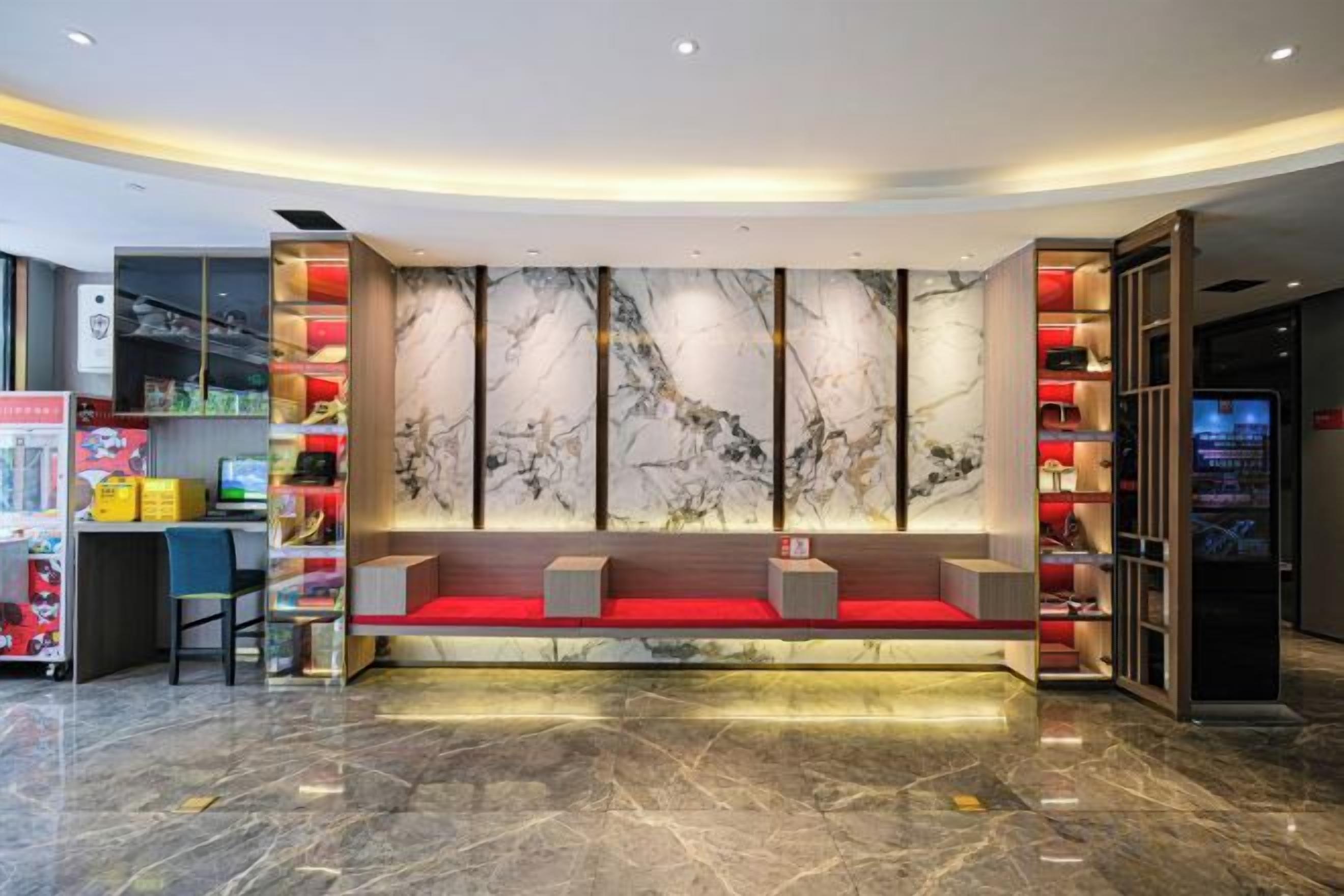 Una hall d'albergo con una reception in marmo, un'area salotto e un chiosco informazioni digitale.