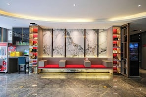 Un hall d’hôtel doté d’un comptoir d’accueil en marbre, d’un espace salon et d’un kiosque d’information numérique.