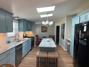 A modern kitchen with blue cabinets, a marble island, and a black refrigerator.