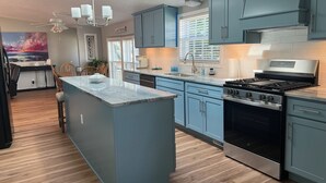 A modern kitchen with blue cabinets, a central island, a built-in stove, and a ceiling fan. - Cozy Chippewa Lake Ranch just steps from the lake! Kayaks and SUPs Private beach (Chippewa Lake)