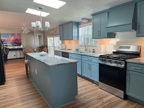 A modern kitchen with blue cabinets, a central island, a built-in stove, and a ceiling fan. - Cozy Chippewa Lake Ranch just steps from the lake! Kayaks and SUPs Private beach (Chippewa Lake)