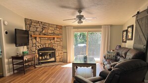 A living room with a stone fireplace, leather sofa, wooden flooring, and a ceiling fan. - Cozy Chippewa Lake Ranch just steps from the lake! Kayaks and SUPs Private beach (Chippewa Lake)