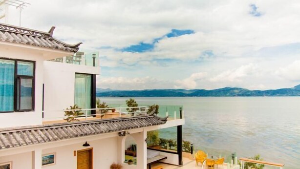 A modern building with a traditional roof, large windows, and a balcony overlooking a body of water. - Dali Huayue Fanxing Sea View Inn (Dali City)