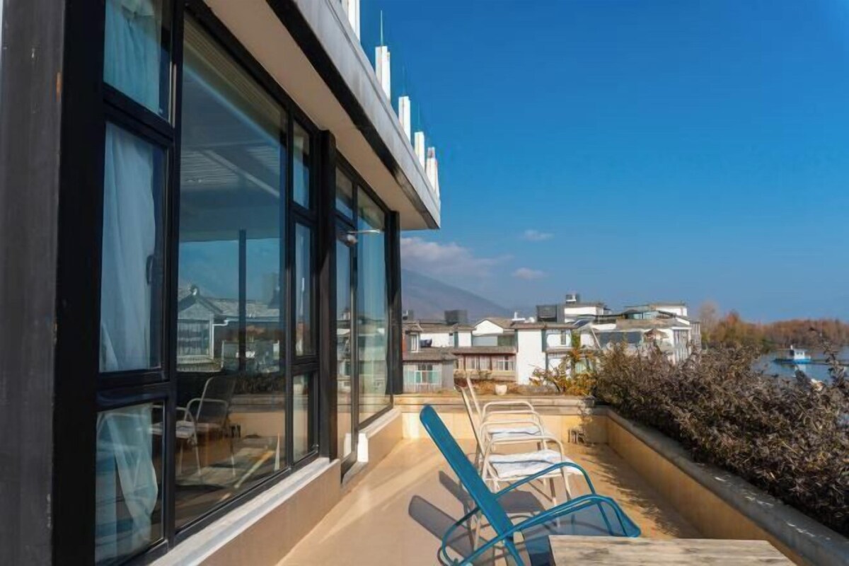 Un edificio moderno con ventanas amplias y un balcón con sillas azules.