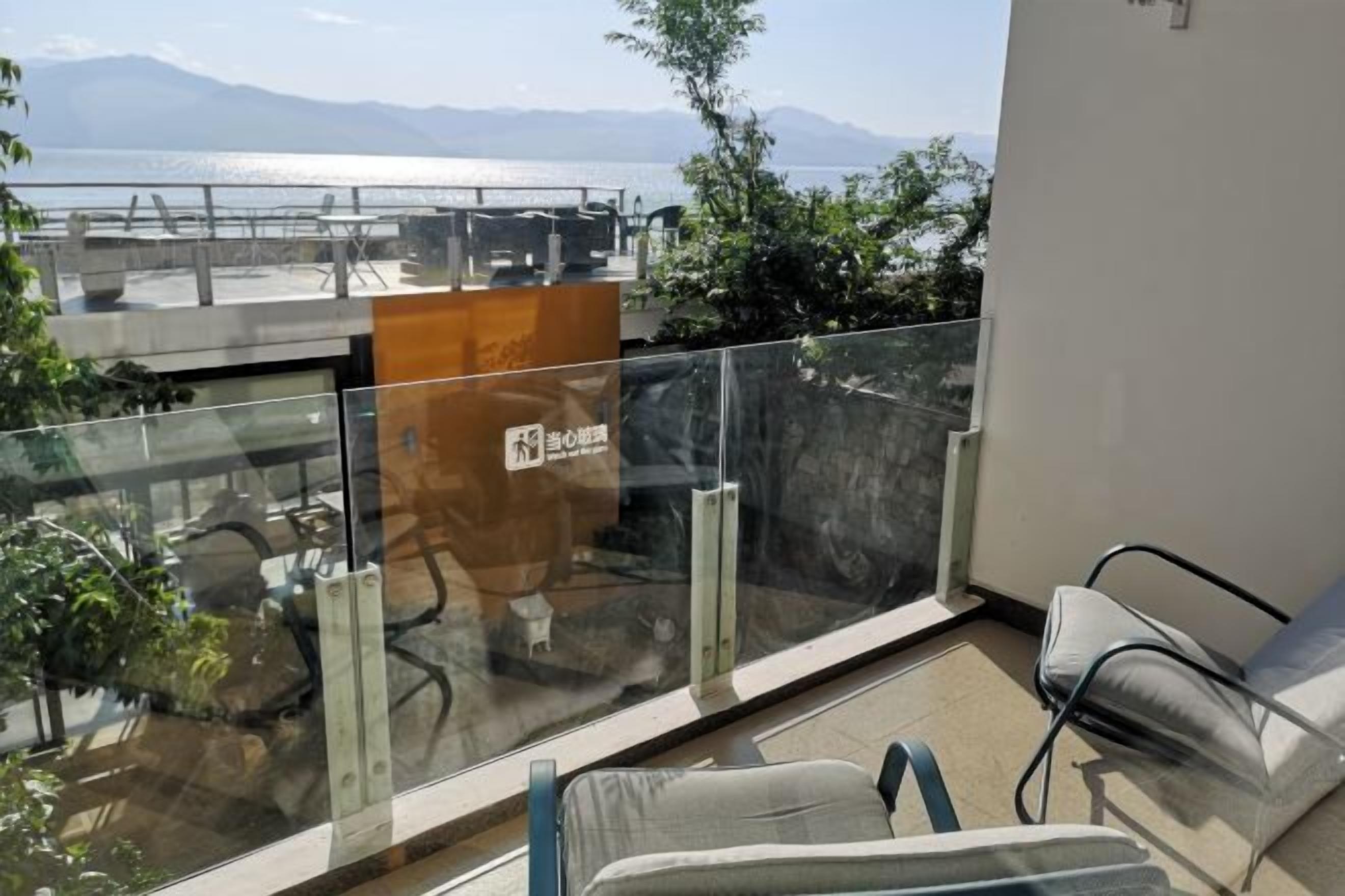 Un balcón con barandilla de vidrio, un sofá y vistas al agua y montañas.