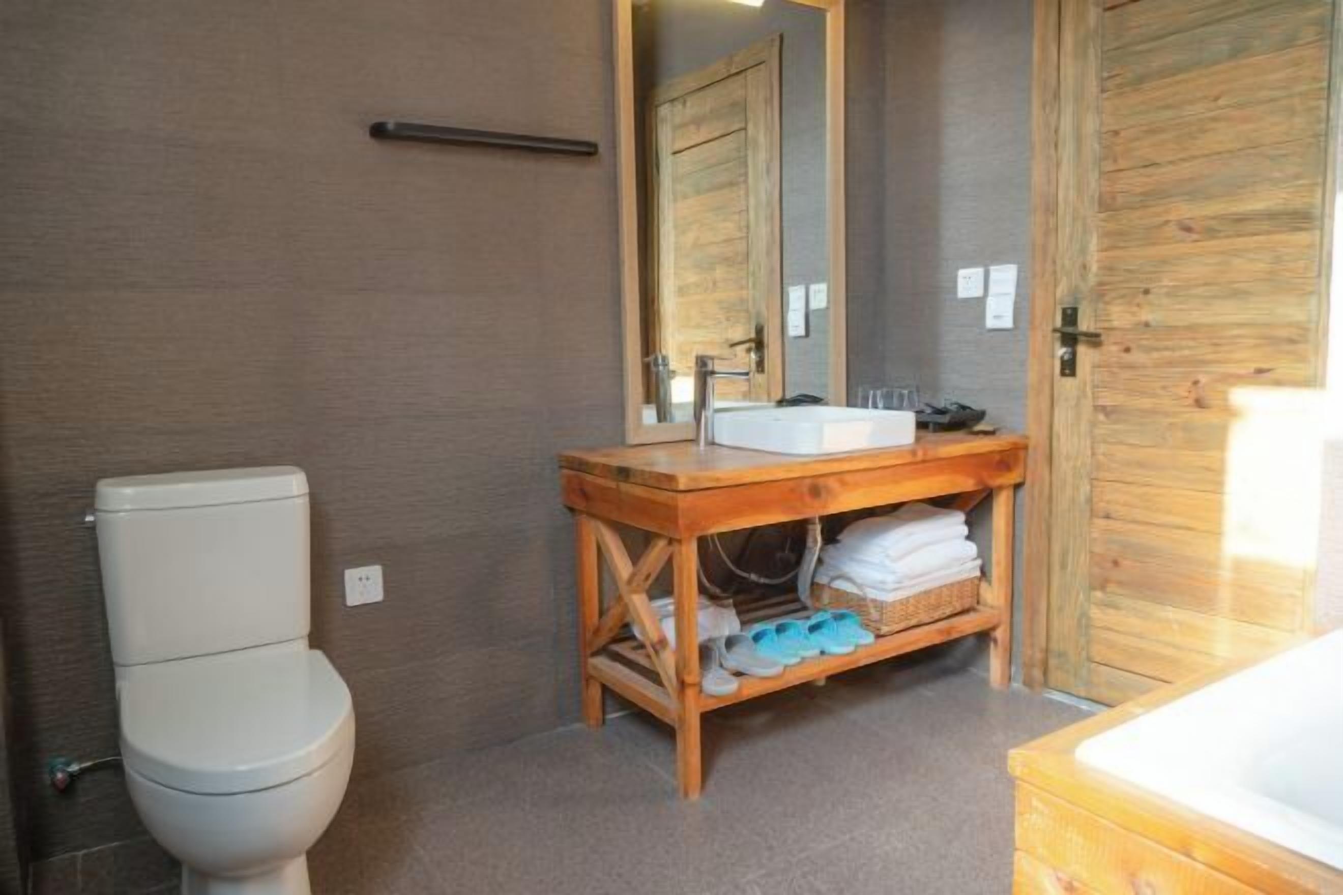 A bathroom with a toilet, wooden vanity, sink, mirror, and a wooden door.