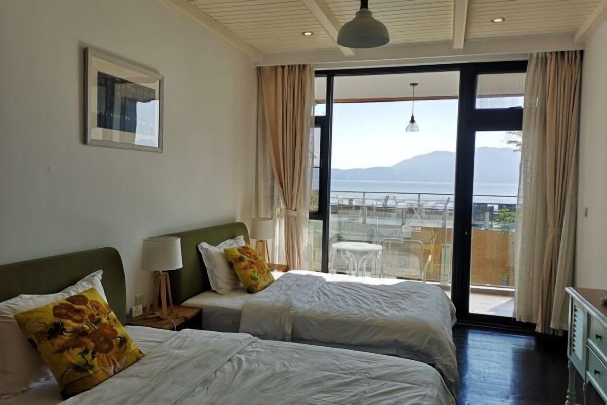 Habitación de hotel con dos camas, un ventanal con vistas al mar y un balcón con mesa y sillas.