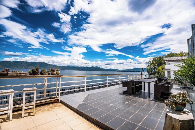 A terrace with a view of a lake and mountains, featuring a railing, seating, and potted plants.